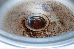Drain of a stainless steel sink for washing dishes is clogged with water and food particles.
